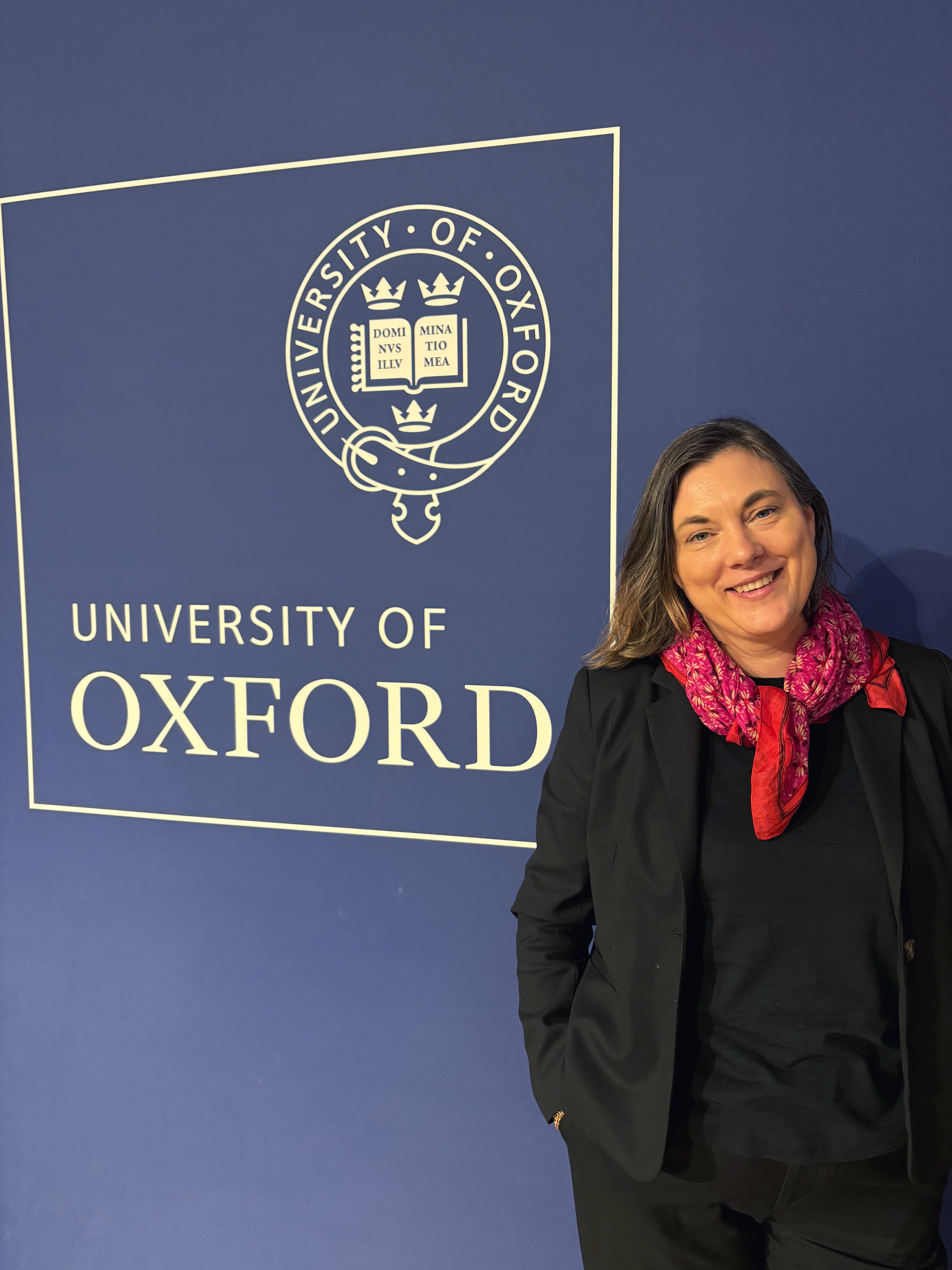 Woman smiling in front of University of Oxford sign