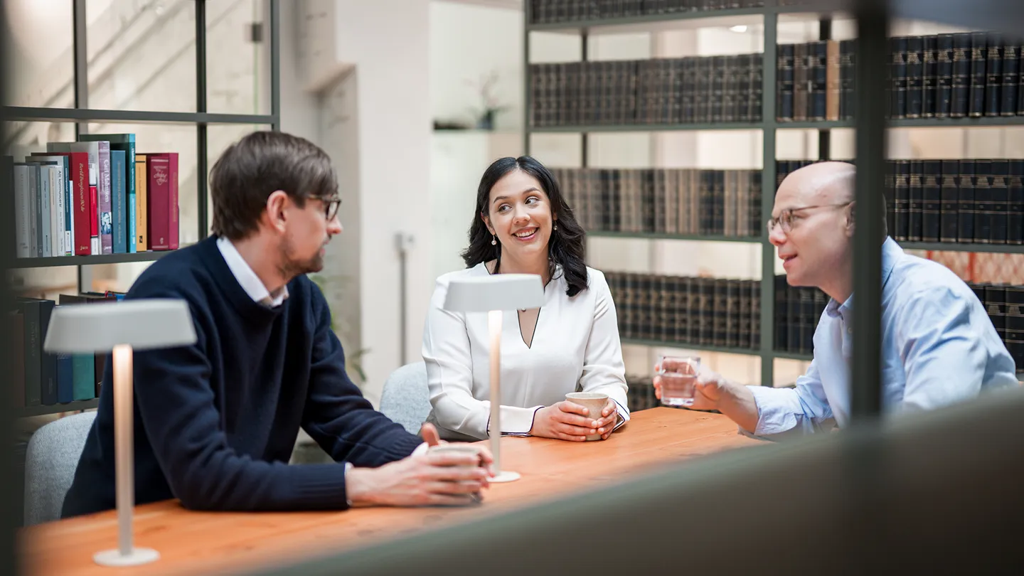 Tre personer sitter och pratar i ett bibliotek