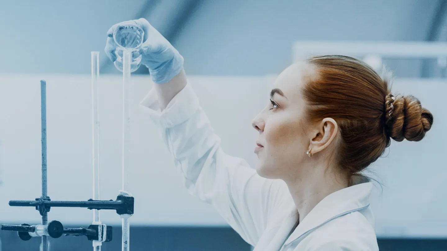 Woman in lab coat pours something into measuring tube