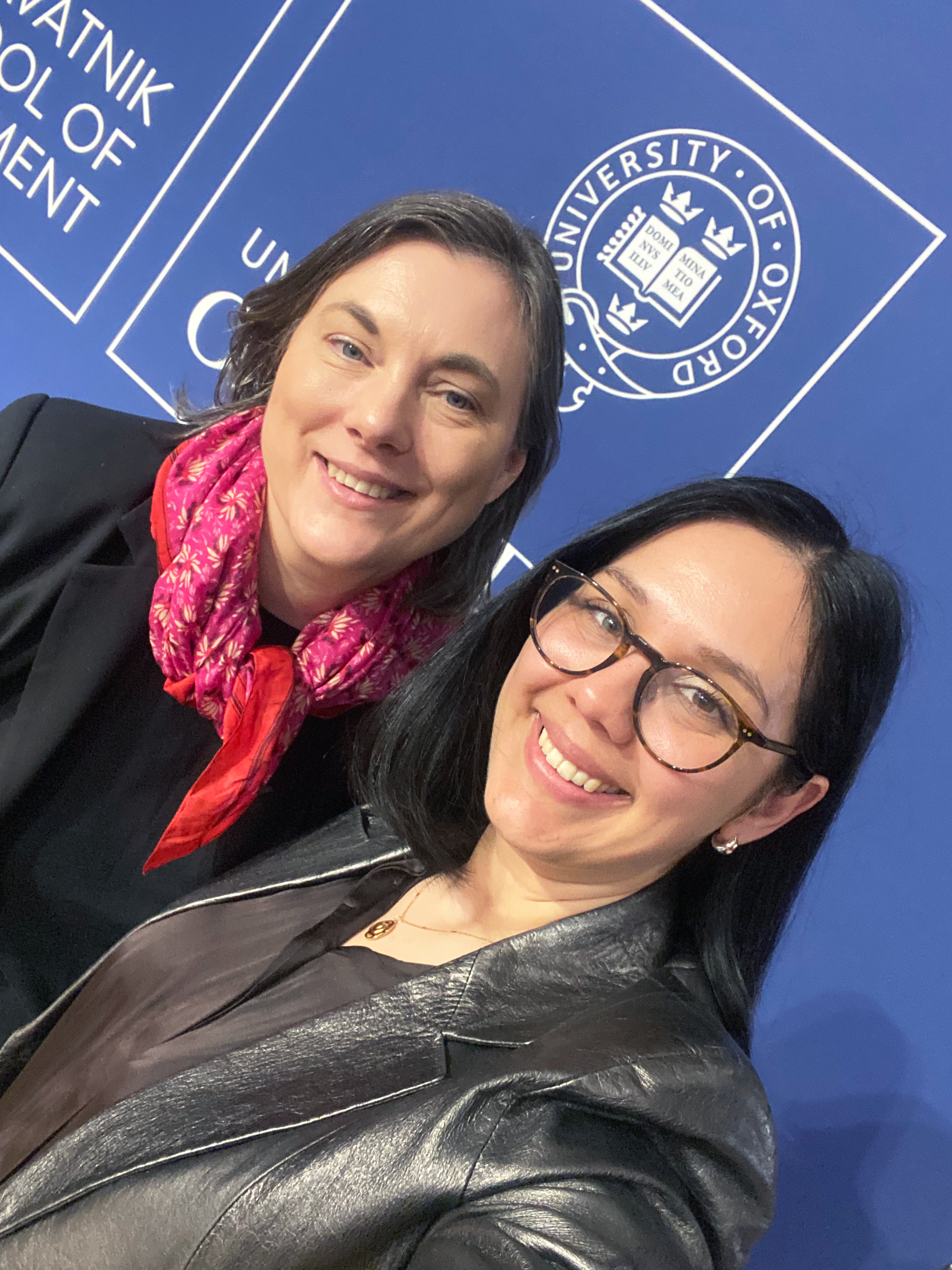 Två leende kvinnor framför University of Oxford skylt